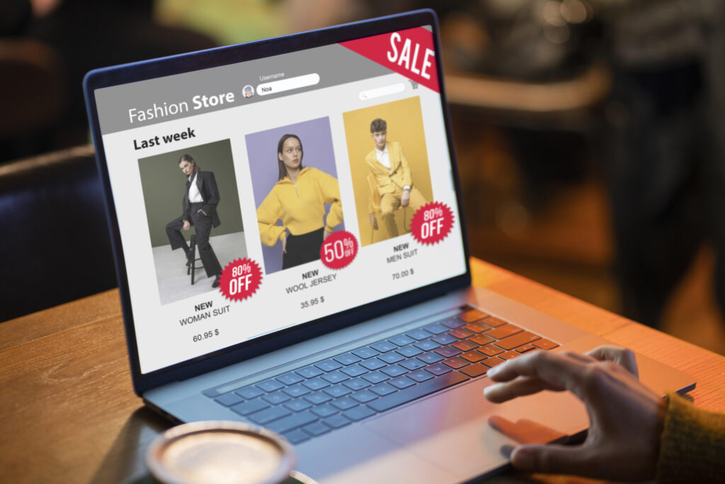Mulher atualizando estoque de roupas em loja de brechó com notebook.