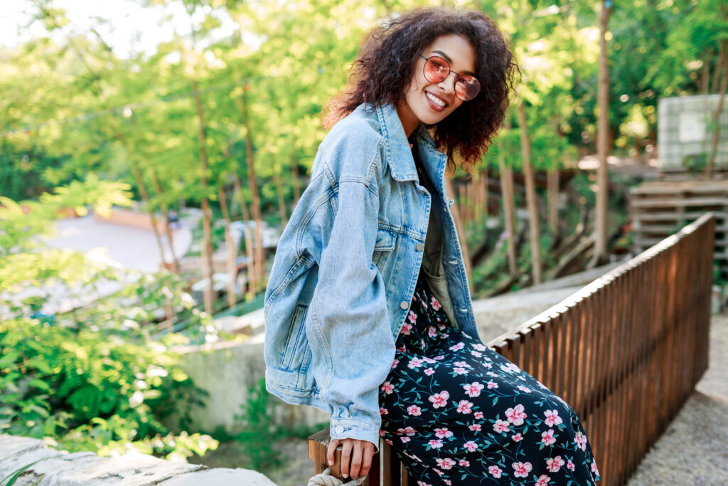 Mulher com look boêmio usando vestido floral e jaqueta jeans oversized.