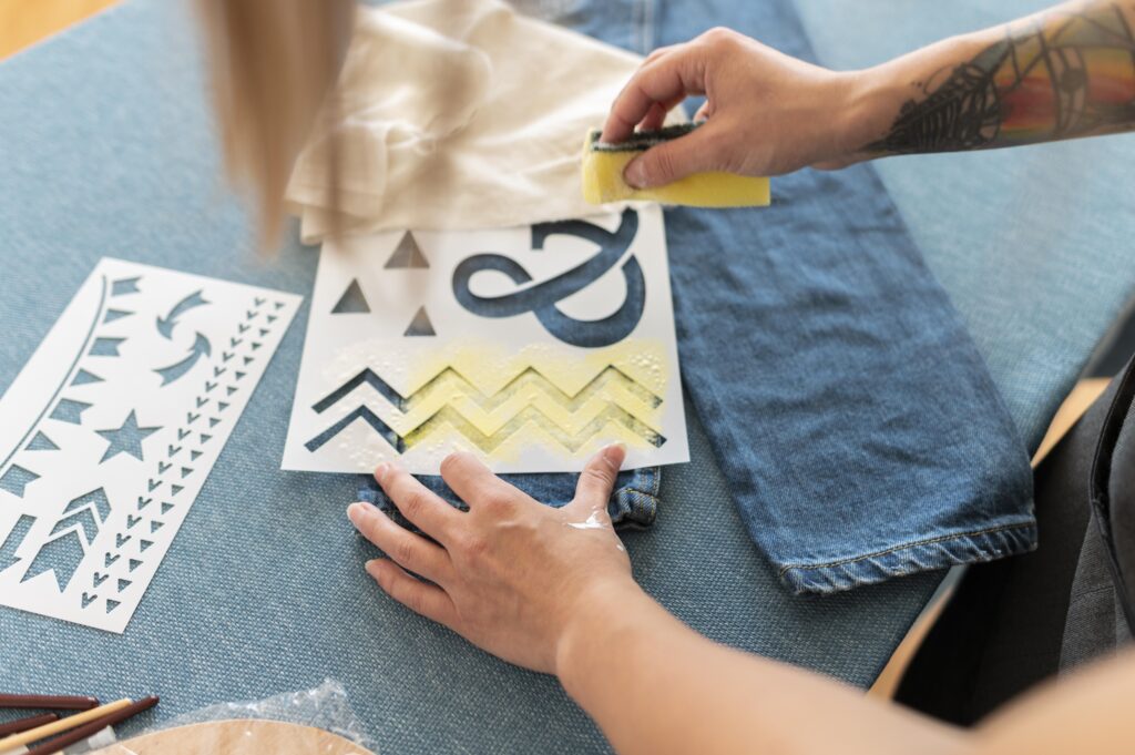 Pessoa realizando upcycling pintando com tinta amarela em uma calça jeans.