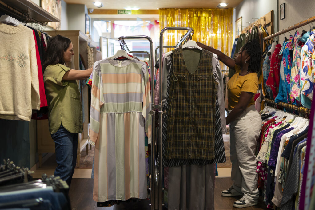 Loja colorida de um brechó brasileiro com roupas penduradas e clientes explorando as peças.