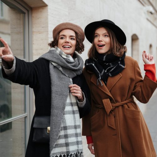 Portrait of two excited girls dressed in autumn clothes walking on a city street